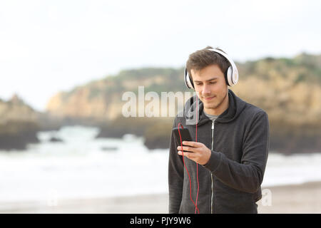 Relaxed teen listening to music with headphones and a smart phone walking on the beach Stock Photo