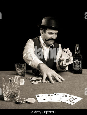 19th century man playing and winning a game of poker drinking a bottle of jack daniel's whisky Stock Photo