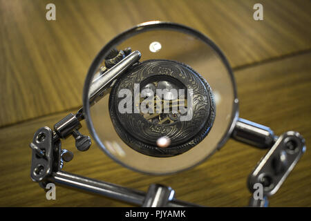 Steel gears of a clockwork mechamism of a vintage pocket watch on a wooden table seen through a magnifying glass Stock Photo