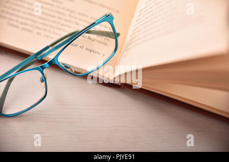 Detail of eyeglasses on open book on white table .Concept need glasses to read. Top view. Horizontal composition Stock Photo