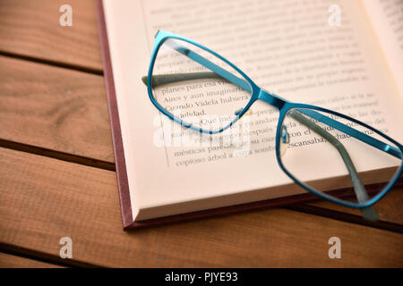 Detail of eyeglasses on open book on top of a natural wood-lined table .Concept need glasses to read. Top view. Horizontal composition Stock Photo