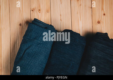 Roll Frayed jeans or blue jeans denim collection on rough wooden table background with copy space, old fashion style concept. Stock Photo