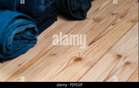 Roll Frayed jeans or blue jeans denim collection on rough wooden table background with copy space, old fashion style concept. Stock Photo