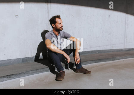 thoughtful caucasian man leaning against a concrete wall looking sad Stock Photo