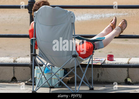 Woman with her feet up on the railings on the Harbour Arm on the seafront in Margate, Kent, England, UK. Stock Photo