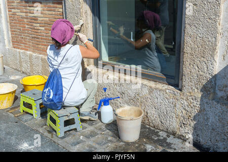 A woman using a mallet and chisel to chip into the stone wall at the front of a shop in Rome, Italy. Stock Photo
