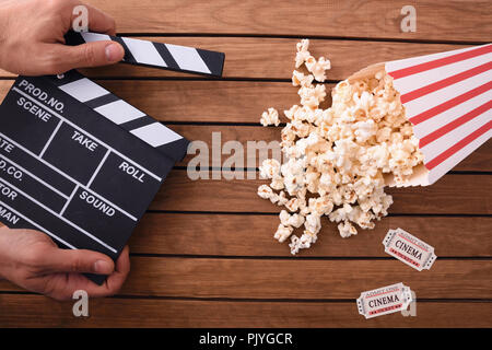 Concept of watching cinema with hand with clapperboard and popcorn on brown wooden background. Horizontal composition. Top view. Stock Photo