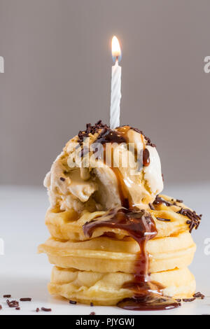 Ice cream and waffle birthday treat drizzled with chocolate syrup and sprinkles with one lit candle - Selective focus side view image Stock Photo