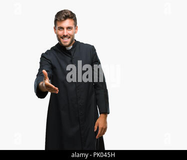 Young catholic christian priest man over isolated background smiling friendly offering handshake as greeting and welcoming. Successful business. Stock Photo