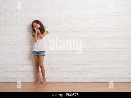 Young hispanic kid stading over white brick wall sleeping tired dreaming and posing with hands together while smiling with closed eyes. Stock Photo