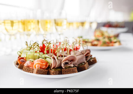 rye bread sandwiches, canapes, bruschetta on white plate. solemn banquet. Lot of glasses champagne or wine on the table in restaurant. buffet table with lots of delicious snacks. Stock Photo