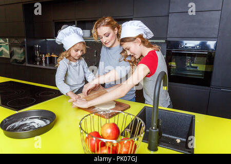 Happy family in kitchen. Mother and two children preparing dough, bake apple pie. Mom and daughters cooking healthy food at home and having fun. House Stock Photo
