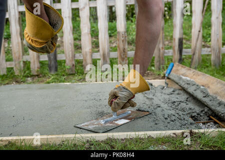 Closeup view of a workman in protective gloves doing plastering or leveling a concrete surface outside in back yard in a construction concept. Stock Photo