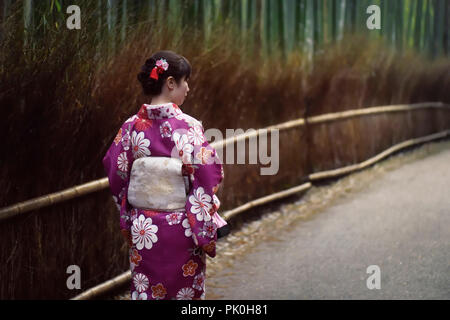 Japanese woman in a purple kimino walking through Arashiyama bamboo forest in Kyoto, Japan.