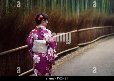 License and prints at MaximImages.com - Young Japanese woman in a purple kimino walking along Arashiyama bamboo forest in Kyoto, Japan.
