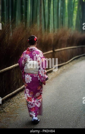 Young Japanese woman in a purple kimino walking along Arashiyama bamboo forest in Kyoto, Japan.