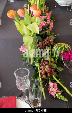 A floral arrangement of lovely orange flowers with colourful pink bunch in foreground with an enticing round watermelon & grapes. Stock Photo
