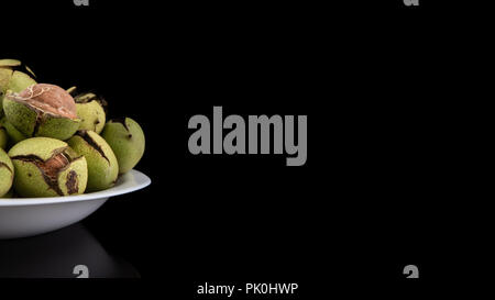 Green walnuts in the plate on a black background, cracked peel, fresh kernel Stock Photo
