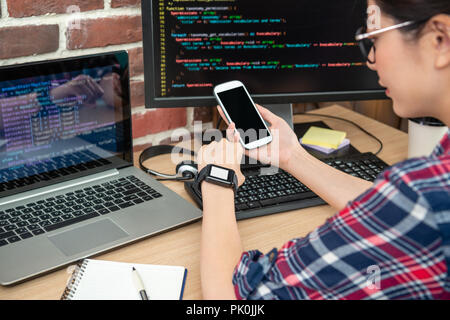 female programmer checking her phone and getting to know the accurate time of her smartwatch. Stock Photo