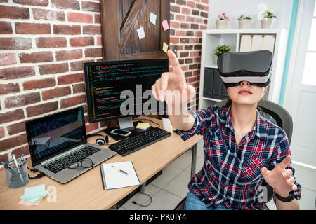 asian woman wearing virtual reality and raising arm touching air in working studio. Stock Photo