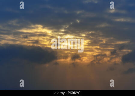 Sun rays breaking through the dark clouds at sunset. Background Stock Photo