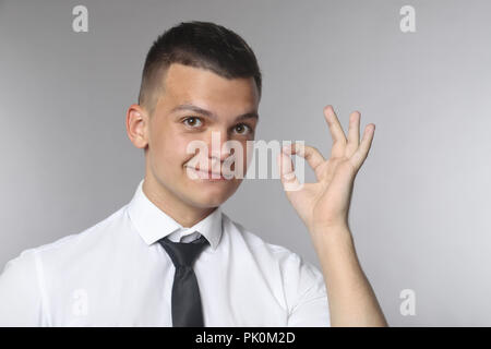 Happy young man in shirt and tie gesturing OK sign and smiling Stock Photo
