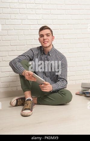 Young man sits with textbooks on the floor against a brick wall background Stock Photo