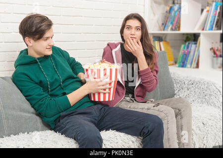 Two teenagers are sitting on the couch watching TV and eating popcorn Stock Photo