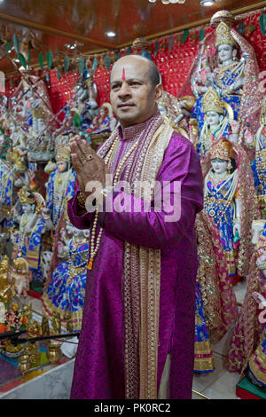 Posed portrait of a Hindu pandit in a small temple in the basement of his home where he leads a congregation. In South Richmond Hill Queens, New York. Stock Photo