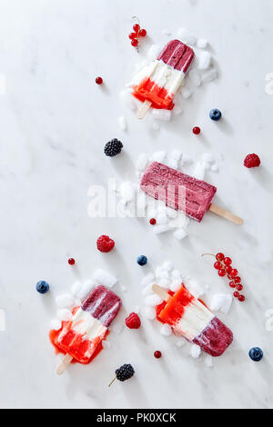 Tricolor strawberry and raspberry ice cream popsicles over ice with berries on marble background, top view and copy space Stock Photo