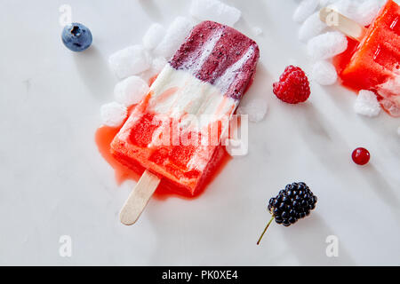 Ice cream popsicles from homemade greek yogurt and fresh organic berries over ice with berries on marble background, top view Stock Photo