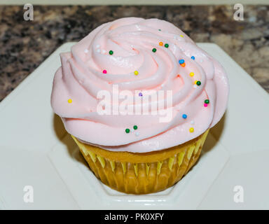 Light pink butter cream frosting swirled on top of fresh homemade cupcake. Colorful candy sprinkles sprinkled on top. Delicious sweet treat for party. Stock Photo