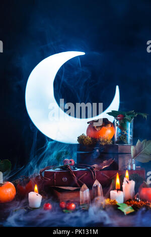 Halloween persimmon with shining full Moon. Witch or wizard workplace with burning candles. Spooky still life concept on a dark background with copy s Stock Photo