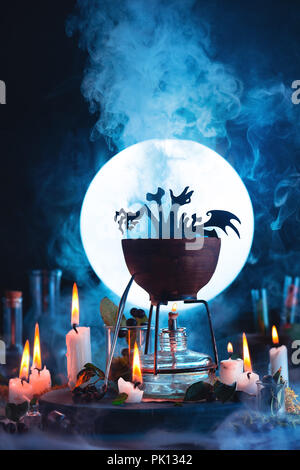 Halloween concept with a cauldron silhouette in front of full Moon. Magical potion with rising steam on witch or wizard workplace. Conceptual still li Stock Photo