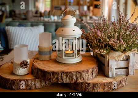 White burning lantern, heather in wooden box on a wooden table decorated in autumnal style, pine cornes, walnuts and candles in rustic style, the concept of autumn. Wedding decor Stock Photo