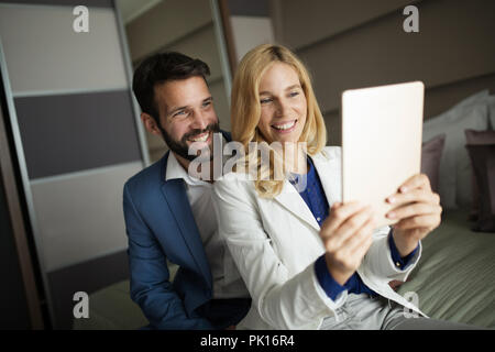 Businessman and businesswoman sitting on bed and using tablet Stock Photo
