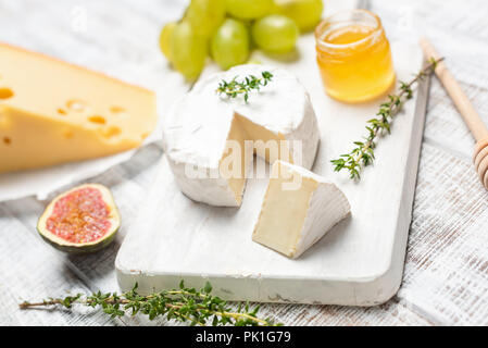 Brie or camembert cheese on white wooden board served with honey, green grapes and figs Stock Photo