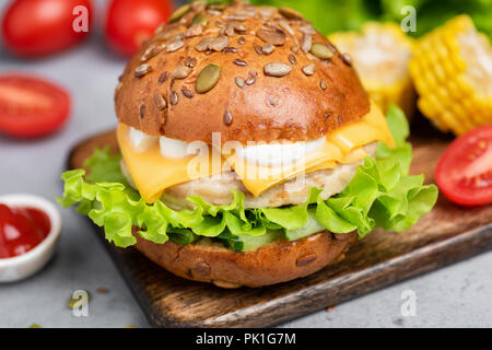 Chicken burger with cheese, lettuce and sauce on wooden serving board. Closeup view. Tasty juicy burger