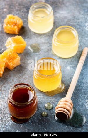 Different types of honey. Acacia, buckwheat honey, wild and raw honey in small jars with wooden honey dipper on dark background Stock Photo