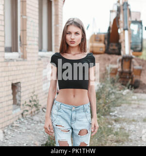Beautiful girl in torn jeans on a construction site near the excavator. Stock Photo