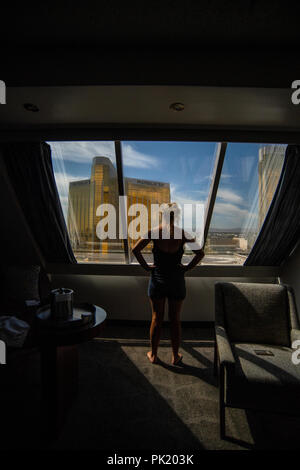 A woman looks out of a hotel room in the Luxor Hotel and Casino towards the Mandalay Bay and Delano resorts in Las Vegas, Nevada, USA. Stock Photo