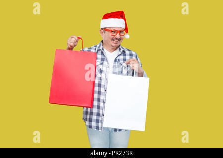 Happy modern middle aged man in casual style and red new year santa cap, eyeglasses and shirt, holding shopping packages with toothy smile, looking at Stock Photo