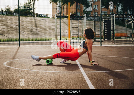 theme sport and rehabilitation sports medicine. Beautiful strong slender Caucasian woman athlete uses foam roller green field street workout to workou Stock Photo