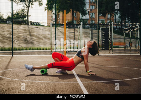 theme sport and rehabilitation sports medicine. Beautiful strong slender Caucasian woman athlete uses foam roller green field street workout to workou Stock Photo