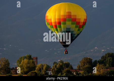 Colorful hot-air balloon flies over typical village in the Tuscan countryside in the light of the sunset Stock Photo