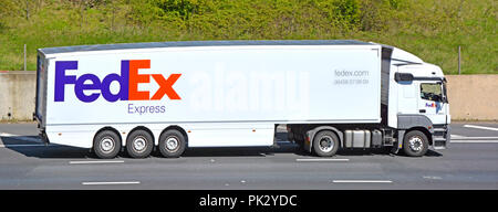 Side view FedEx Express transport delivering packages & freight via hgv lorry truck articulated white trailer & logo driving along motorway England UK Stock Photo