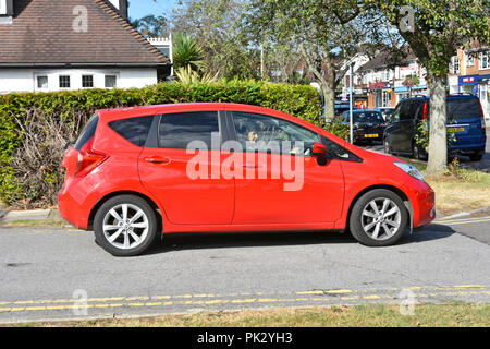 Mature senior woman car driver side view driving five door red Nissan Note hatchback tinted back window glass in an urban location Essex England UK Stock Photo