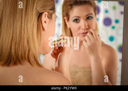 Young woman applying lipstick on her lips in front a mirror in the bathroom at home. Stock Photo