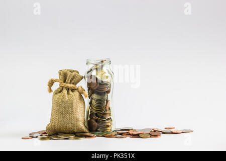 Saving money for future concept : Sack bags, full money coins in jar glass and on ground on white background. Stock Photo