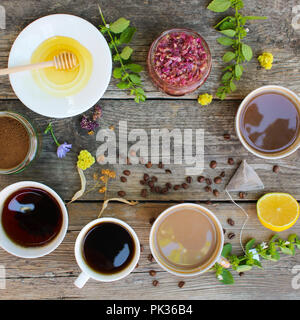 Tea, coffee, cocoa in cups, chicory, lemon, mint, jam made of rose petals, dried lime, honey on the old wooden background. Top view. Stock Photo